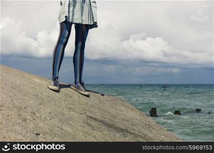The legs of a young woman as she is standing by the coast