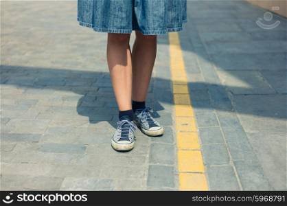 The legs of a young woman as she is standing in the street by a yellow road marking line