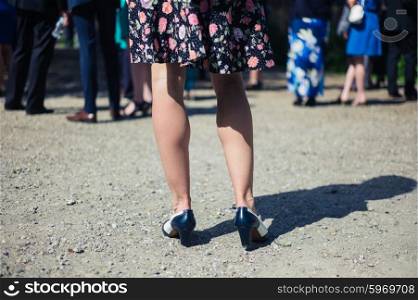 The legs of a young woman as she is standing outside in a rural setting with people participating in a social event