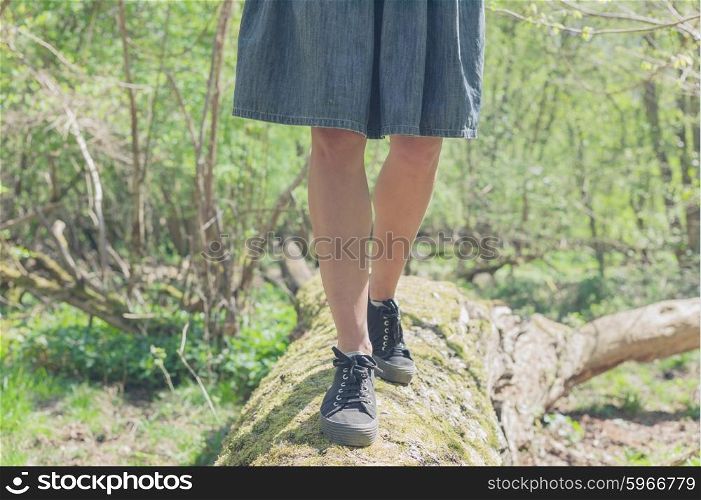 The legs of a young woman as she is walking on a felled tree in the forest on a sunny day