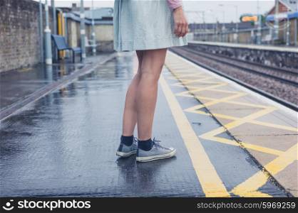 The legs of a young woman standing on a platform waiting for the train
