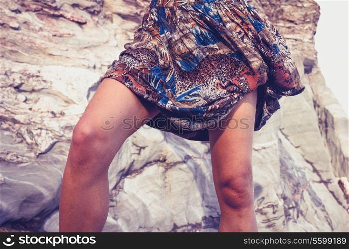The legs of a young woman standing outside near a rock