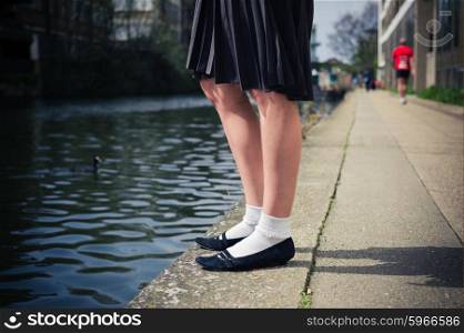 The legs of a young woman wearing a skirt as she is standing by a canal on a sunny day