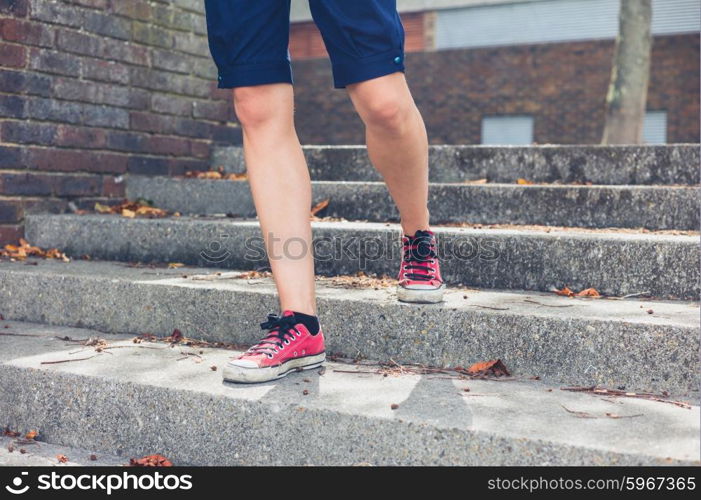 The legs of a young woman wearing shorts as she is walking down some steps outside