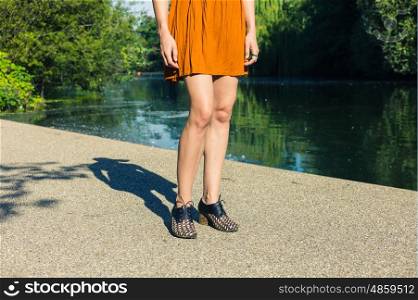 The legs of a young woman who is standing by a pond in the park on a sunny summer day