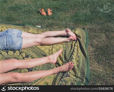 The legs of two young women as they are relaxing on the grass outside on a sunny day