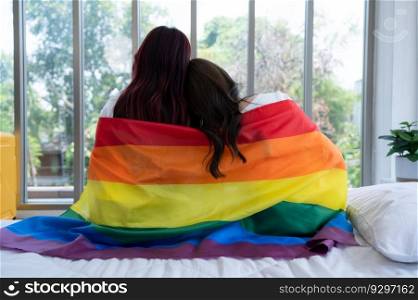The LGBT couple sat on the bed, covered in rainbow flags, peering out the window to observe the nature in the hotel room.