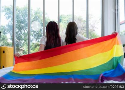 The LGBT couple sat on the bed, covered in rainbow flags, peering out the window to observe the nature in the hotel room.