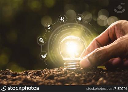 The light bulb was placed on the ground and there was a man&rsquo;s hand holding while there was a technology icon around it.