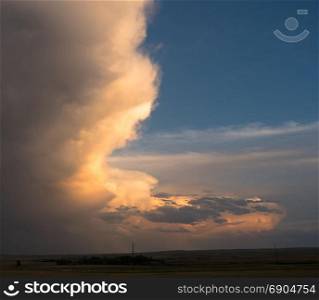 The light from a sun dropping low on the horizon hits a storm cloud near sunset