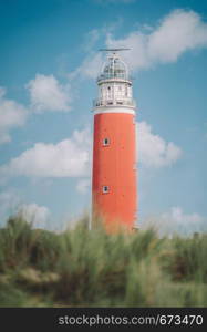 The lighthouse of the island of Texel in The Netherlands surrounded by tall sand dunes in beautiful sunlight and cloudy sky