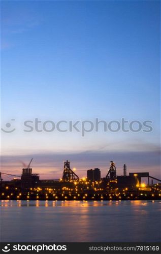The lights at an industrial steel works plant in contrast with the blue sky of the setting sun at dusk