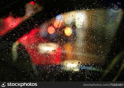 The lights of the big city at night through the glass of the car covered with raindrops