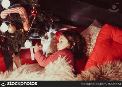 The little dark-haired girl lying on the floor near the gifts and Christmas tree. Little girl near a Christmas tree