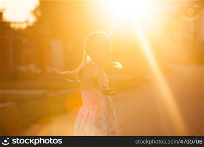 The little girl enjoys the sunset, she looks up and spreads his hands with pleasure