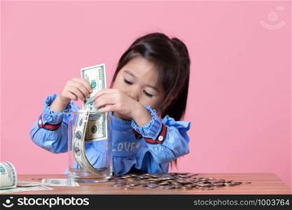 The little girl is putting the banknote in a clear glass jar, Money saving concept.