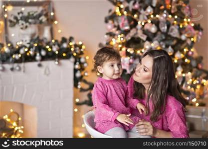 The little girl next to her mother, surrounded by Christmas light.. Portrait of mother with daughter on the Christmas tree in sparkling lights