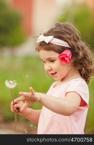 The little girl with a red flower in her hair played with dandelion. Curly girl with dandelion