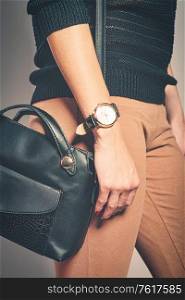 The lovely lady poses with a black leather bag on her shoulder and wears a massive gold watch on her arm. The lovely lady poses with a black leather bag on her shoulder and wears a massive gold watch
