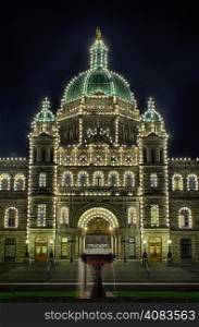The main entrance and dome of the British Columbia Parliament Building in Victoria as illuminated at night with lights that outline the shape of the building.