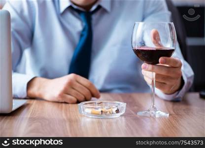 The male employee drinking alcohol and smoking cigarettes at workpla. Male employee drinking alcohol and smoking cigarettes at workpla