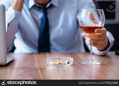 The male employee drinking alcohol and smoking cigarettes at workpla. Male employee drinking alcohol and smoking cigarettes at workpla