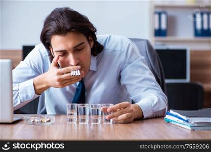 The male employee drinking vodka and smoking cigarettes at workplace. Male employee drinking vodka and smoking cigarettes at workplace