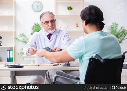 The male patient in wheel-chair visiting old doctor. Male patient in wheel-chair visiting old doctor