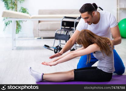 The male physiotherapist doing exercises with injured woman on floor. Male physiotherapist doing exercises with injured woman on floor