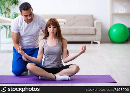 The male physiotherapist doing exercises with injured woman on floor. Male physiotherapist doing exercises with injured woman on floor