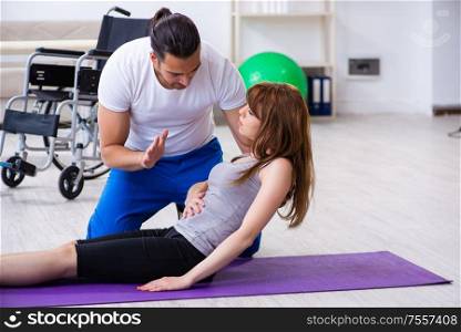 The male physiotherapist doing exercises with injured woman on floor. Male physiotherapist doing exercises with injured woman on floor