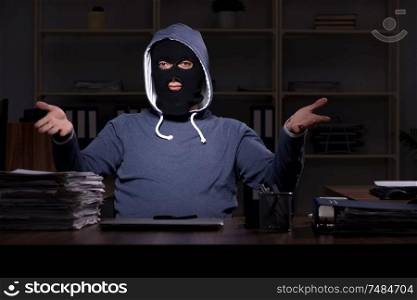 The male thief in balaclava in the office night time . Male thief in balaclava in the office night time