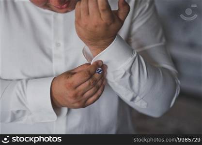 The man carefully fastens the cufflinks on his shirt.. The process of fastening cufflinks on the sleeves of a white shirt 2361.