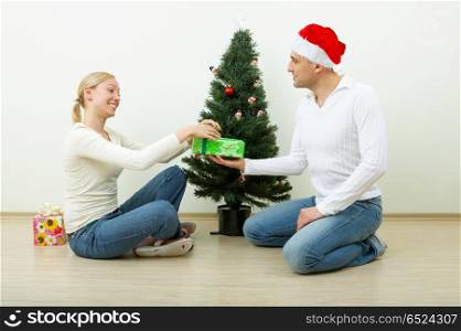 The man gives a gift to the woman against a Christmas pine. Gift