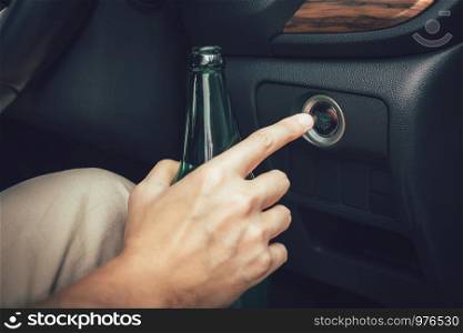 The man hand is holding a beer bottle and pressing the engine start button.