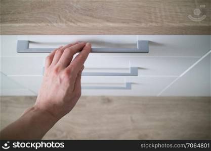 The man hand is open is in the white kitchen cabinet with drawer. detail man hand is open of a laminate stylish kitchen drawer