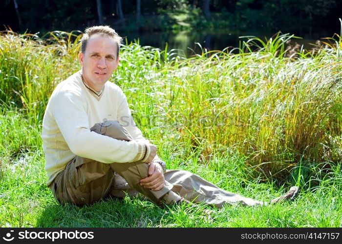 The man in a beige jumper on the bank of a pond