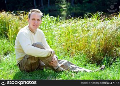 The man in a beige jumper on the bank of a pond