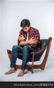 The man in a striped shirt sits sick and sits on a chair and crosses his arms.