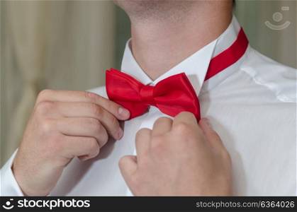 the man in the white shirt tying a red bow tie