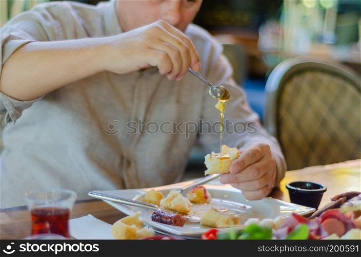 The man is having breakfast with pleasure. He pours honey on the bread.