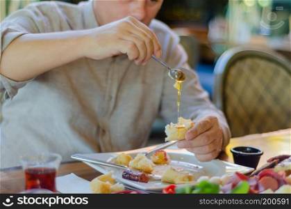 The man is having breakfast with pleasure. He pours honey on the bread.