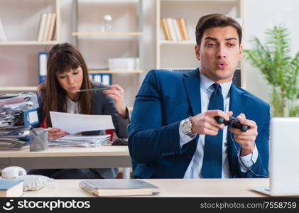 The man playing games in office while colleague is busy. Man playing games in office while colleague is busy