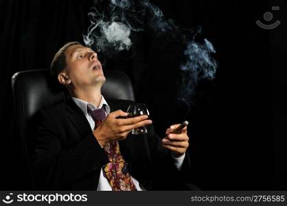 The man with a cigar and a glass of cognac. A dark background