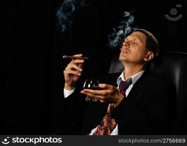 The man with a cigar and a glass of cognac. A dark background