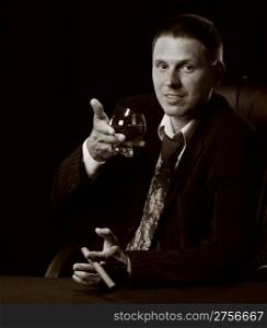 The man with a cigar and a glass of cognac. Monochrome tone. A dark background