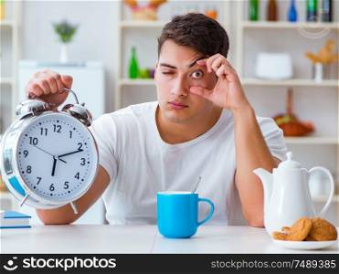 The man with alarm clock falling asleep at breakfast. Man with alarm clock falling asleep at breakfast
