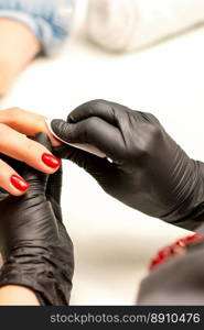 The manicurist finishes the procedure for red nail polishing and cleaning with a cotton napkin, pad, swab in a beauty salon, close up. The manicurist finishes the procedure for red nail polishing and cleaning with a cotton napkin, pad, swab in a beauty salon, close up.