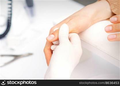 The manicurist holds the female thumb during a manicure procedure in the nail salon. The manicurist holds the female thumb during a manicure procedure in the nail salon.