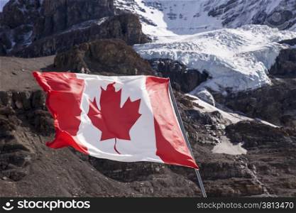 The maple leaf of the Canadian Flag flutters in a brisk wind. In the background, the main glacier of Mount Andromeda tumbles from the summit headwall.